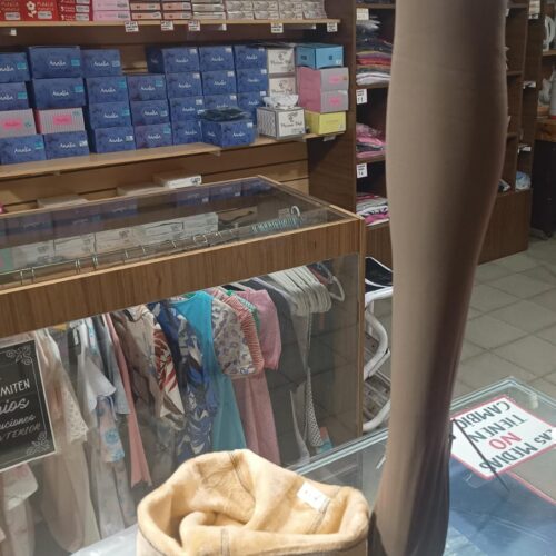 Fotografía profesional del interior de El Rincón de las Medias en San Luis, mostrando pantys térmicas con forro de peluche beige sobre mostrador de vidrio. Incluye maniquí de pierna y estanterías de lencería. Ropa interior de abrigo en Rivadavia 515.